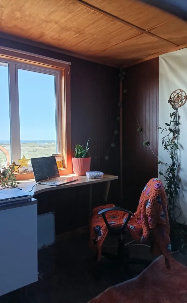 Espacio de trabajo de Maritza: escritorio de madera bajo una ventana luminosa, una silla con manta tejida a crochet y plantas